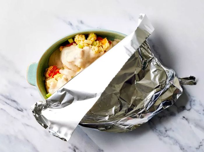 Stuffed pork chops smothered in sauce and covered with foil, ready to bake.