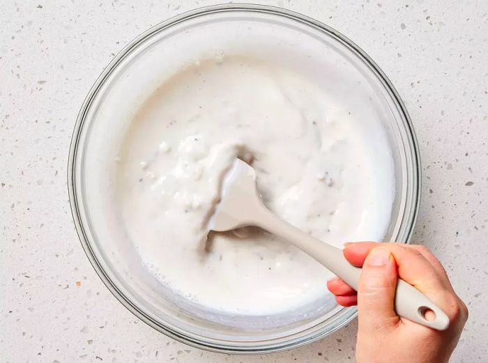 A glass bowl with condensed soup and milk being mixed with a rubber spatula.