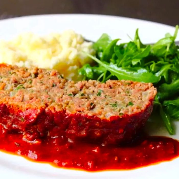 A close-up shot of Meatball-Inspired Meatloaf served with creamy mashed potatoes and a fresh arugula salad on a white plate.