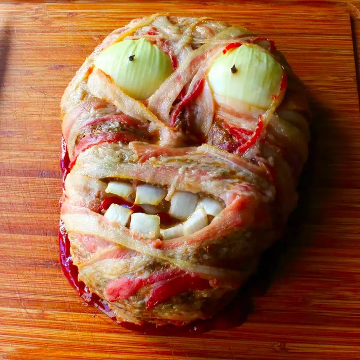 A close-up of the Zombie Meatloaf featuring onion eyes, displayed on a wooden cutting board.