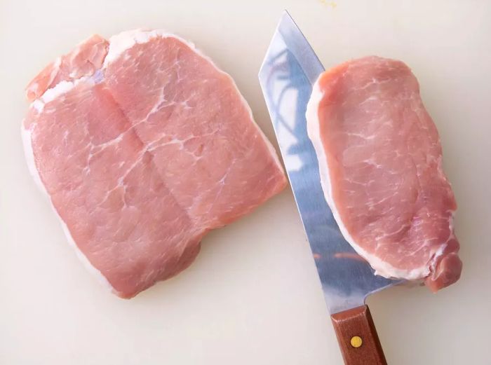 Two pork chops being sliced on a cutting board.