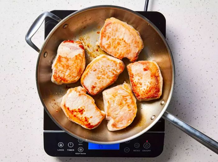 A large skillet filled with six perfectly seared pork chops.