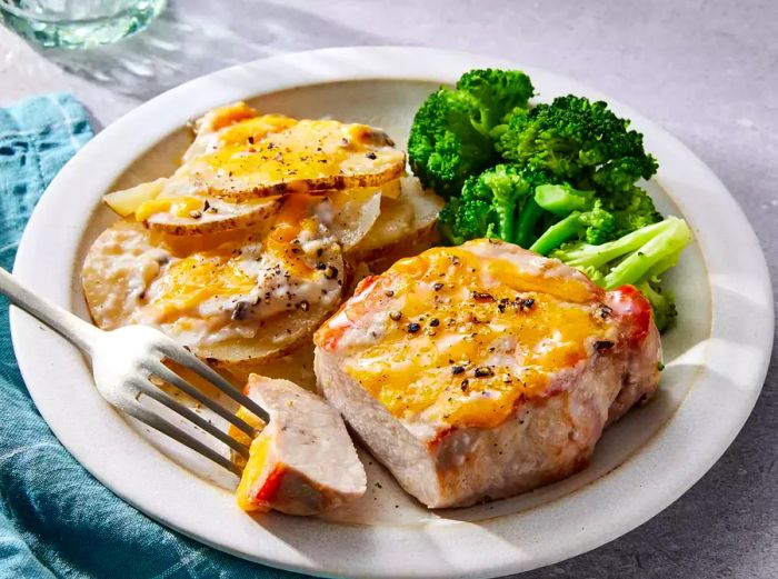 A plated serving of pork chop and potato casserole, accompanied by steamed broccoli.