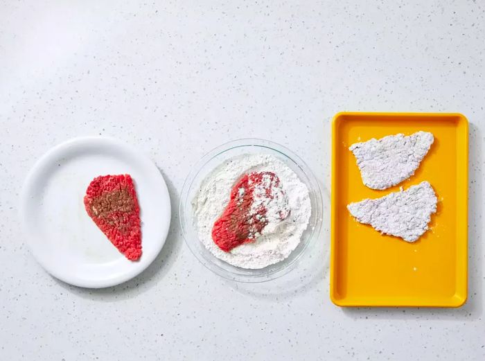 The cube steak is coated in the flour mixture and placed on a tray.