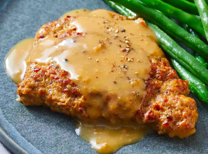 A close-up of a country-style steak, topped with rich gravy, served alongside a portion of green beans.