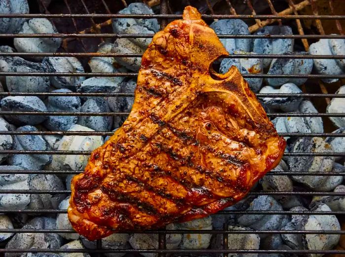 A porterhouse steak grilling over hot charcoal.