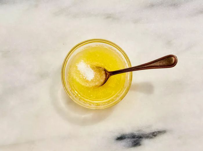 A bowl filled with melted butter and salt, accompanied by a spoon.