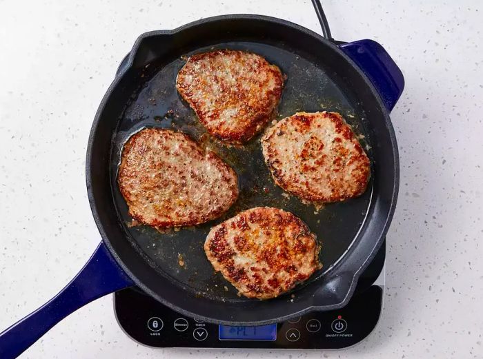 Steaks cooking in hot oil in a skillet, achieving a browned crust on both sides.