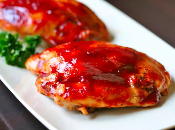 A close-up shot of an oven-baked BBQ chicken thigh on a white plate.