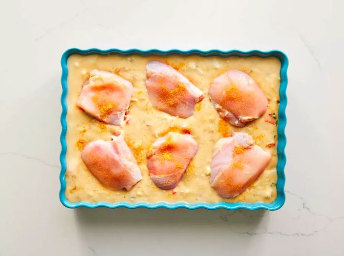 Seasoned chicken thighs placed over the creamy mixture in the baking dish.