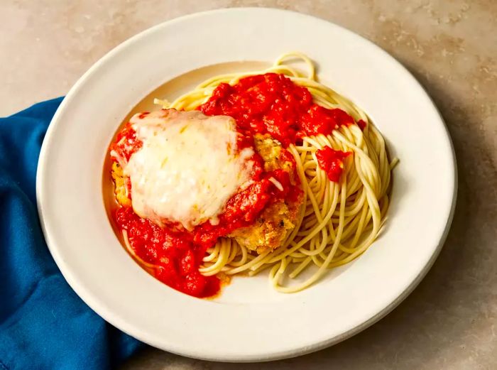 Aerial view of a plate of baked chicken Parmesan served over pasta.