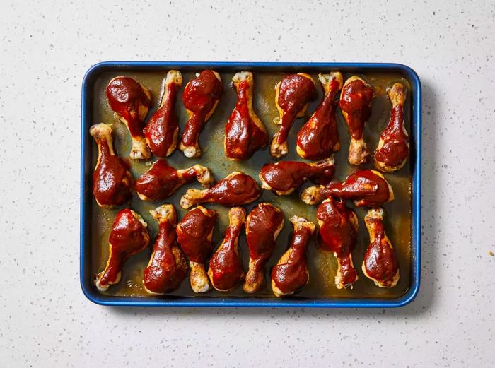 A baking sheet with perfectly baked chicken drumsticks smothered in barbecue sauce.