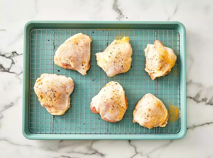 A top-down view of seasoned chicken thighs arranged on a baking rack, ready for roasting