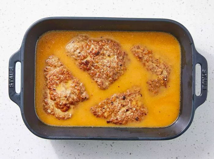 The broth is poured over the steaks in the baking dish.