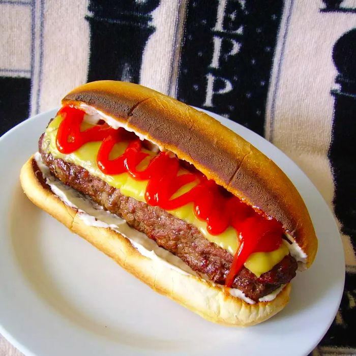 A hot dog-shaped burger with cheese and ketchup served on a bun, plated beautifully.