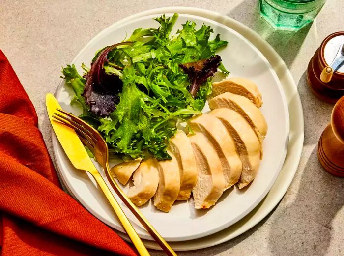 A plate of sliced chicken breast accompanied by a side of mixed greens.