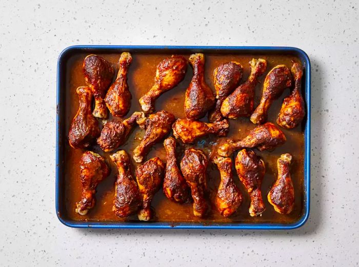 A baking sheet filled with slow-cooked chicken drumsticks, glazed with barbecue sauce.