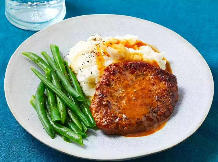 A close-up shot of a plate featuring cube steak served over mashed potatoes, accompanied by a side of green beans.