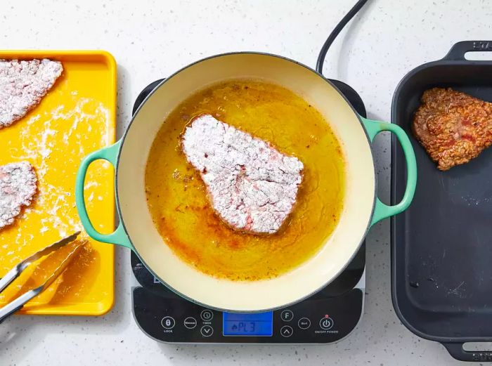 The cube steak is fried until golden brown and then transferred to a baking dish.