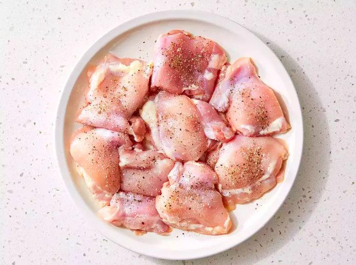 A plate of raw chicken thighs seasoned with salt and pepper