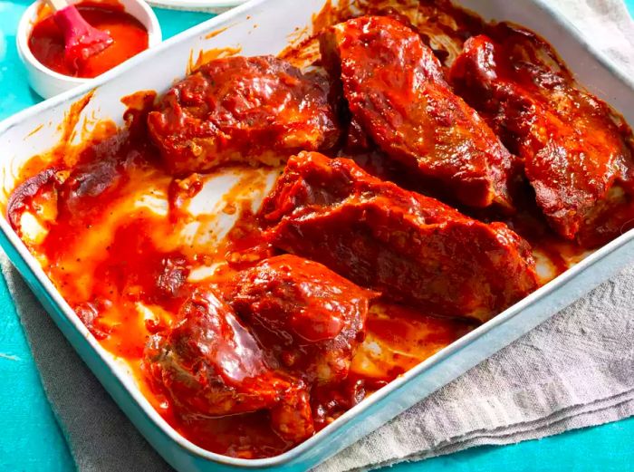 high-angle shot of BBQ ribs smothered in sauce, served in a white baking dish