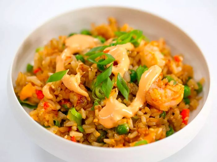 a white bowl filled with shrimp fried rice, garnished with scallions and drizzled with sauce