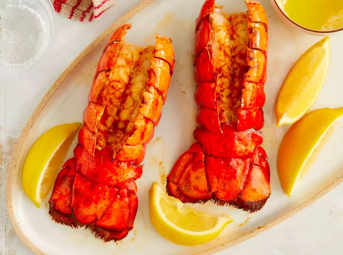 a top-down view of broiled lobster tails served with lemon wedges on a white plate