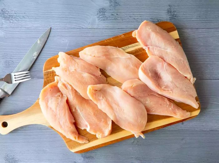 Raw chicken breasts resting on a wooden cutting board.