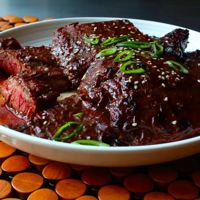 A close-up shot of Grilled Hoisin Beef garnished with fresh herbs, served in a white bowl.