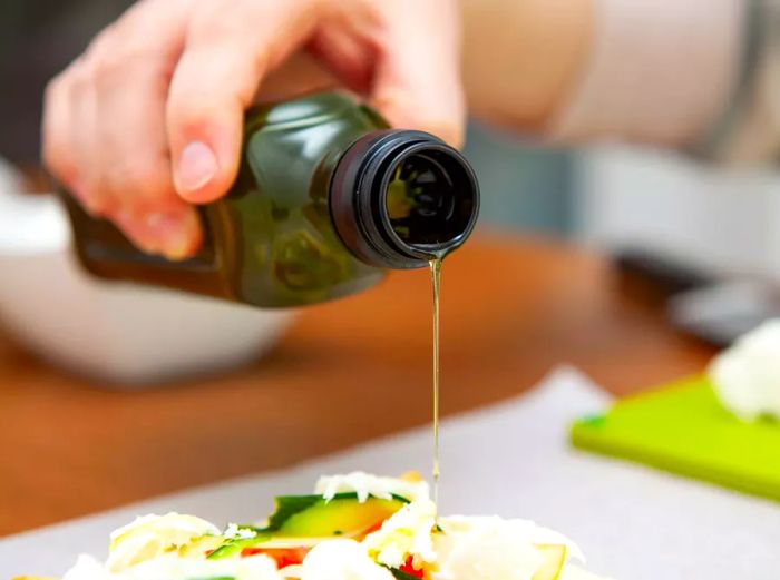 A person holding a bottle of olive oil, drizzling it over a dish.