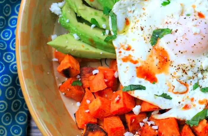 A hearty breakfast bowl with diced sweet potatoes, slices of avocado, ground meat, black beans, and a fried egg