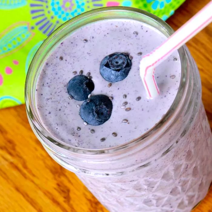 blueberry smoothie topped with three fresh blueberries and a straw