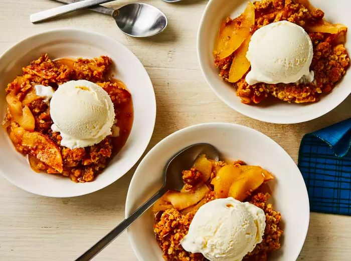 A bird's-eye view of three bowls of apple crisp topped with melting vanilla ice cream