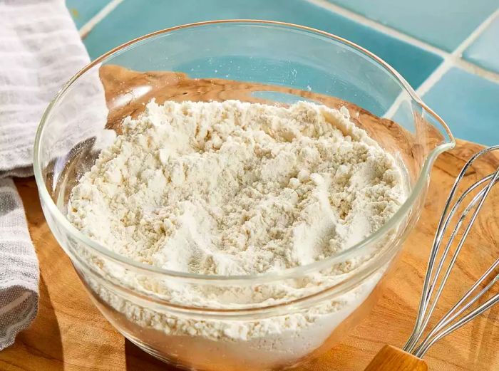 A bowl of self-rising flour beside a whisk