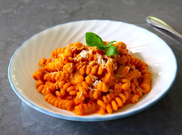 A bowl of curly pasta topped with light red Trapanese sauce and a sprig of fresh basil.