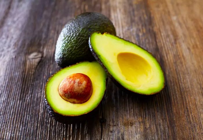 Whole and sliced avocado on a wooden surface