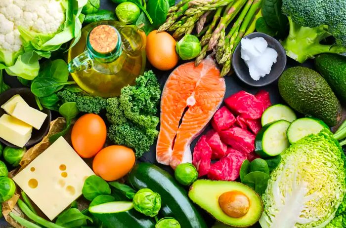 A variety of healthy ketogenic, low-carb ingredients on a kitchen table, including green vegetables, meats, salmon, eggs, and cheese, illustrating the concept of balanced diet nutrition for overall health.