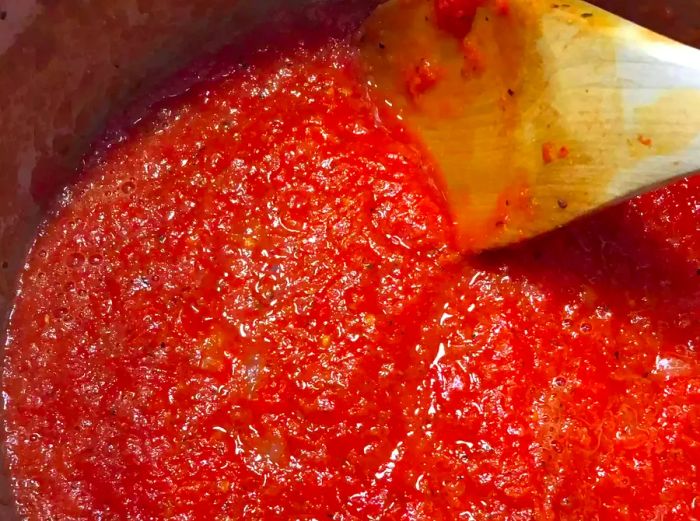 Close-up of freshly made spaghetti sauce simmering in a pot with a wooden spoon