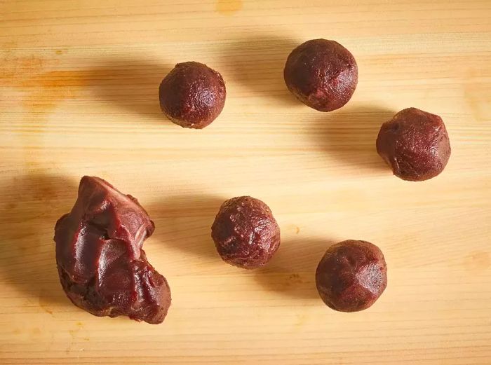 Red bean paste divided into equal portions and rolled into balls on a wooden surface.