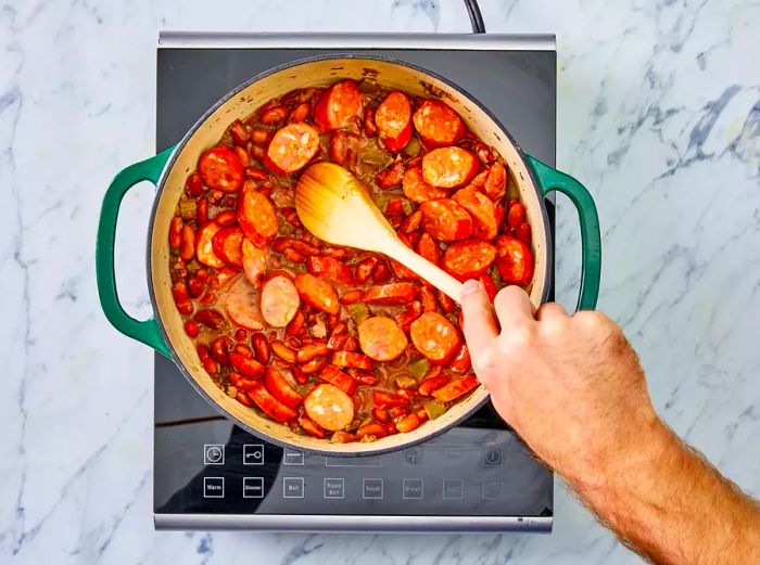 Sausage being stirred into a pot of beans.