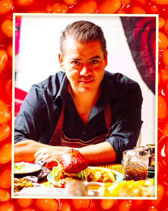 Katsuji Tanabe wearing a black button-down shirt and brown apron, sitting at a table with food.