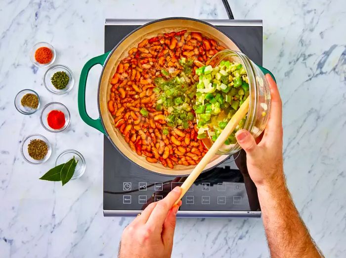 Sautéed vegetables being stirred into the pot of beans.