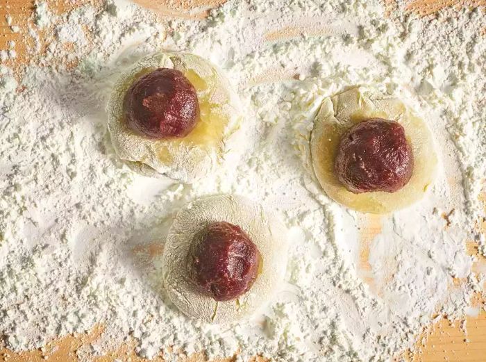 Rice flour and red bean paste being shaped into balls on a surface dusted with flour.