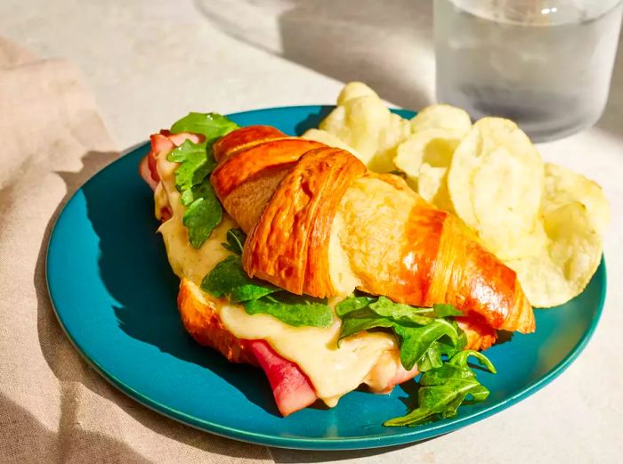 The Ultimate Croissant Sandwich served with chips on a plate