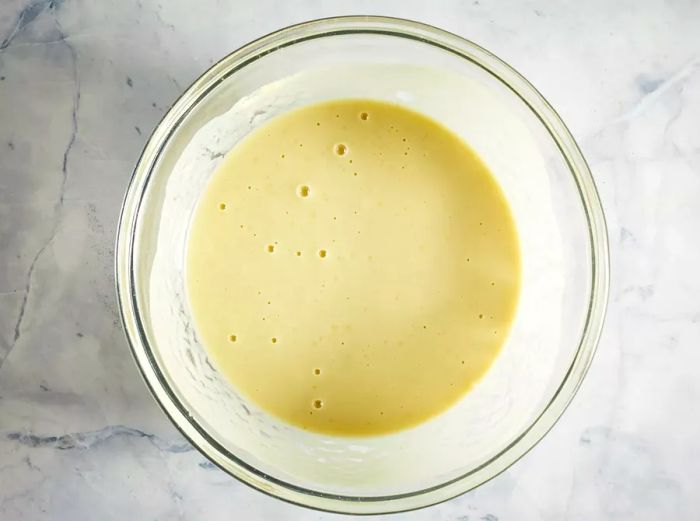 A glass bowl containing glutinous rice flour, green tea powder, water, and sugar mixed together.