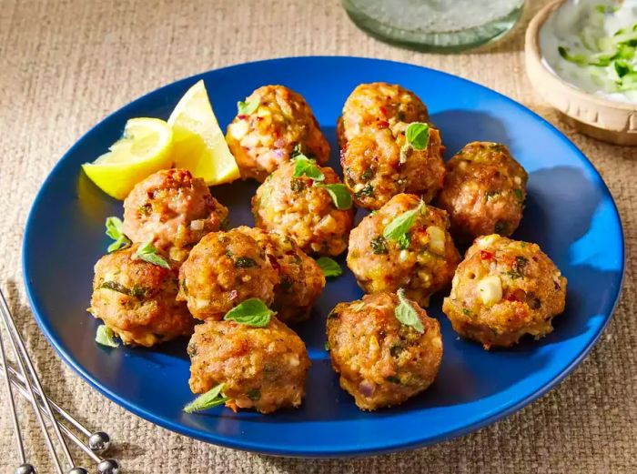 Greek Turkey Meatballs served with fresh herbs and lemon wedges on a blue plate