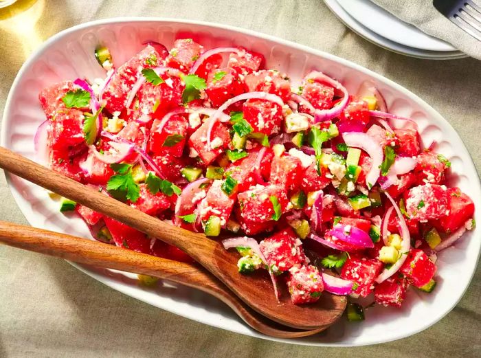 A refreshing watermelon salad with feta cheese, onions, and cilantro, served in a pink dish.