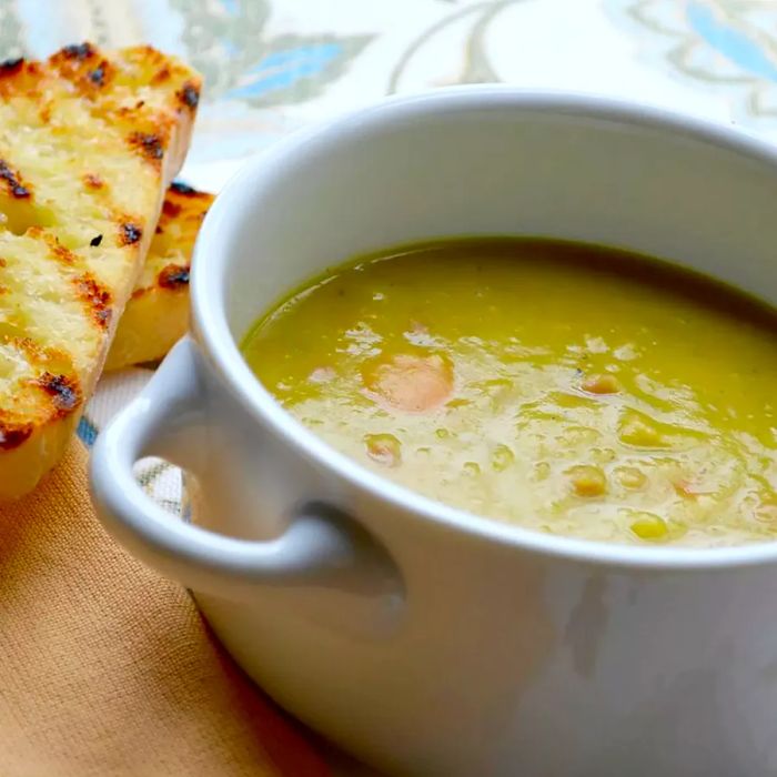 A close-up view of a bowl of ham and split pea soup, served with toasted bread on the side.