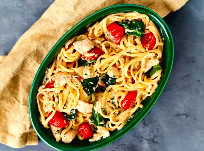 Overhead view of a green oval bowl filled with pasta, chicken, spinach, and grape tomatoes