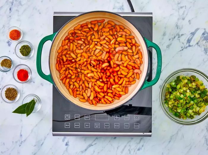 Beans submerged in water in a green Dutch oven.